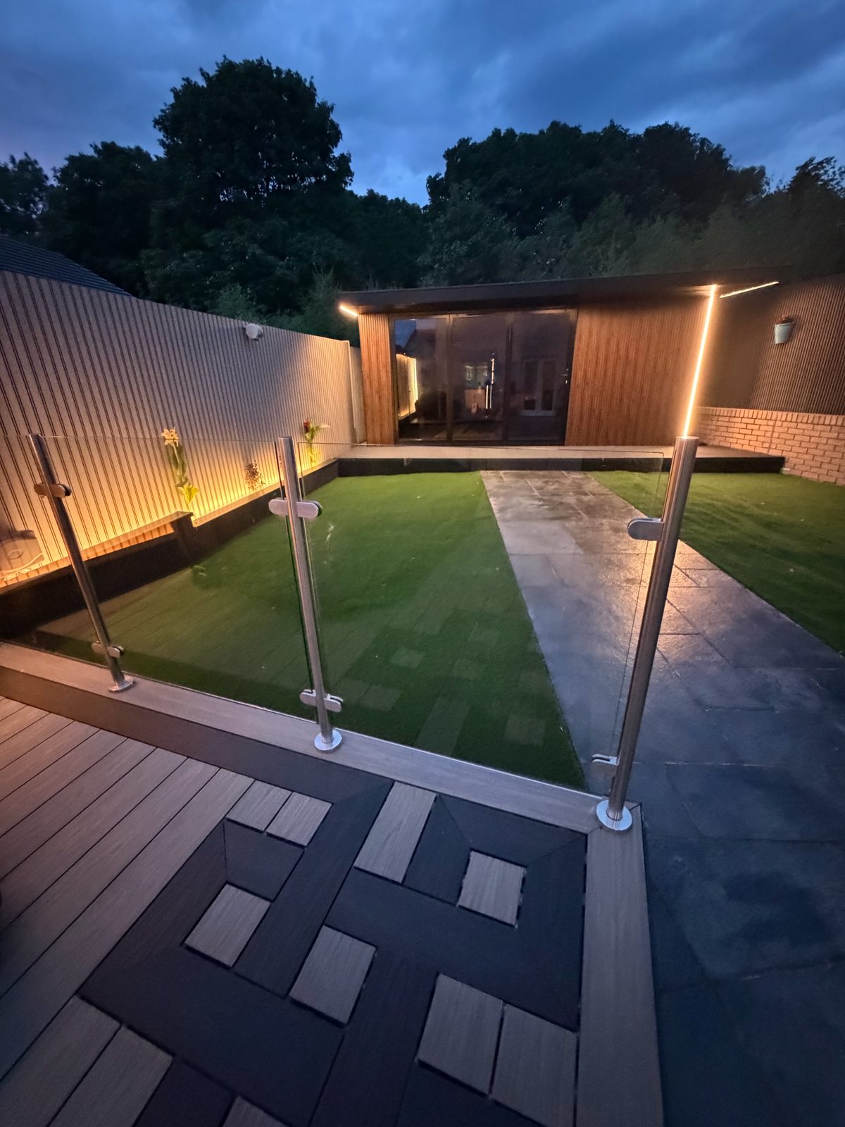 Wooden garden cottage with lit doorway and lawn path at dusk