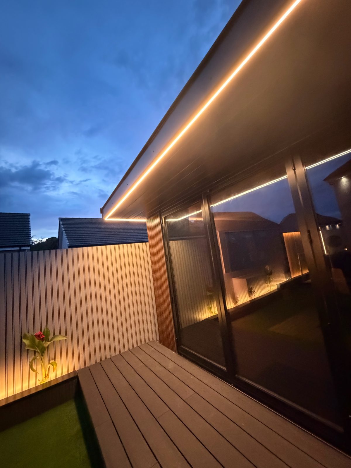 Garden room eave lighting over dark decking at twilight