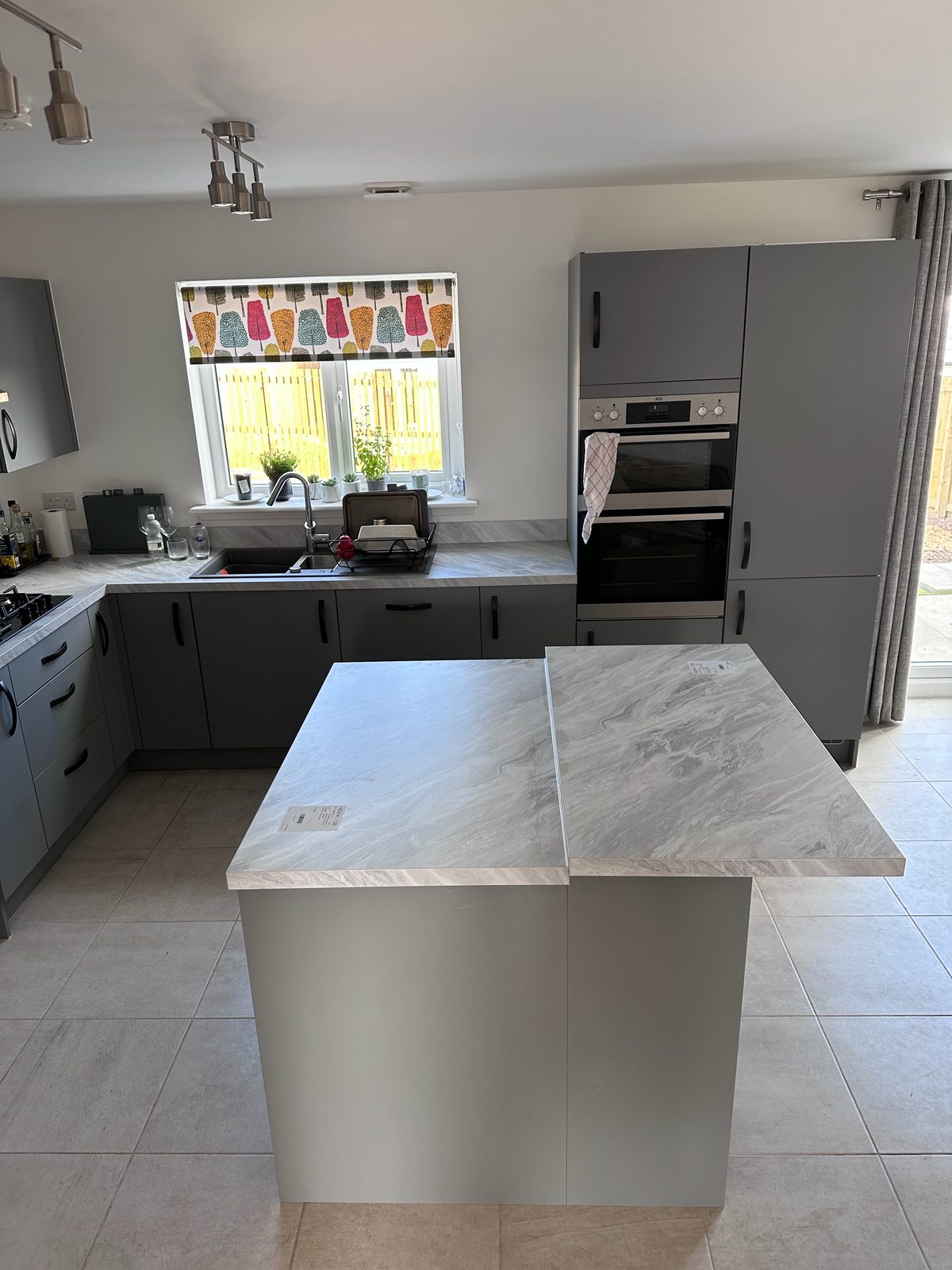 Modern grey kitchen installation by EscapeHaus Joinery — island, marble-effect worktops and tall oven housing