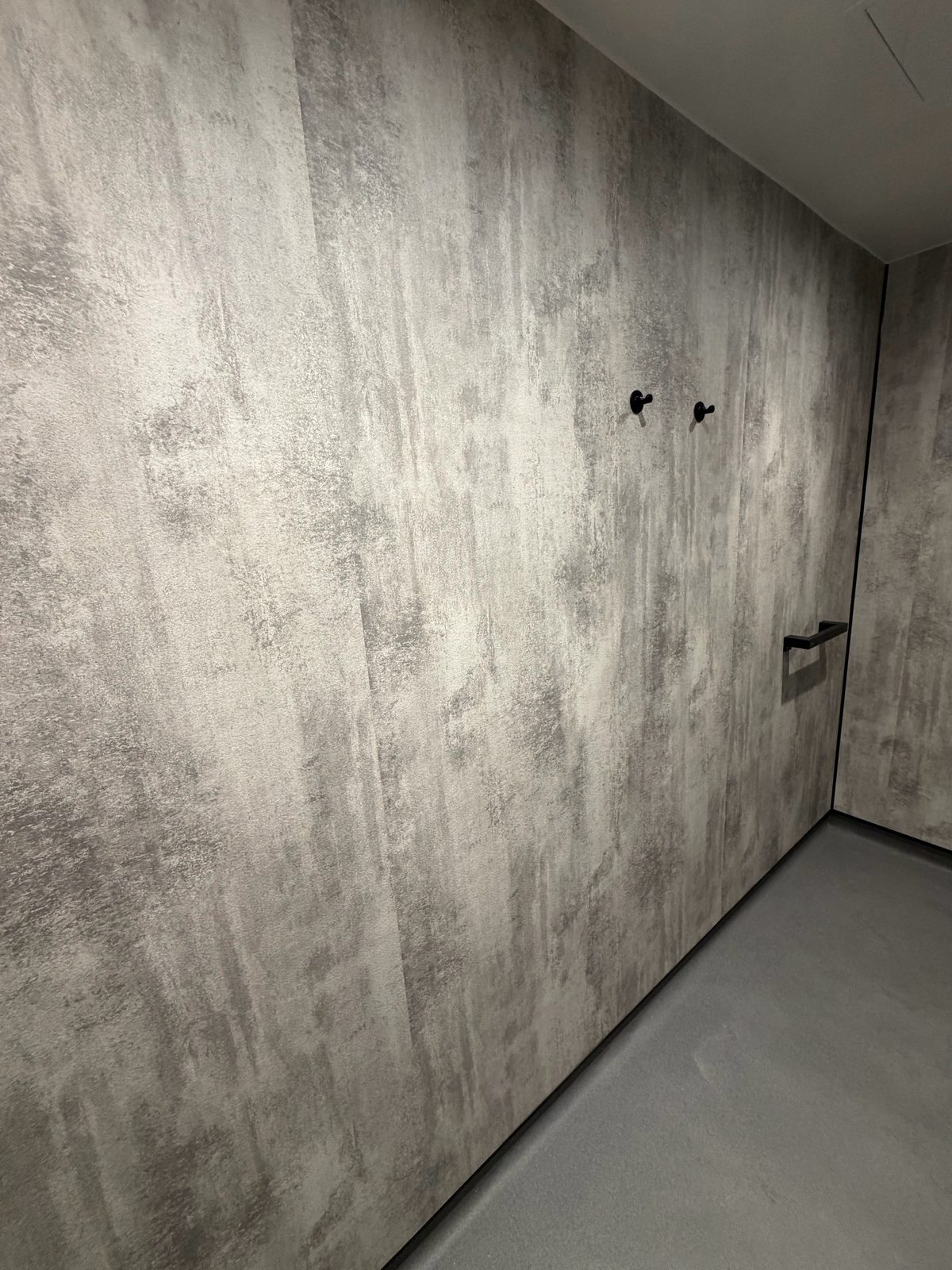 Wet room corner with matte black hooks and grab rail on grey concrete-effect panels