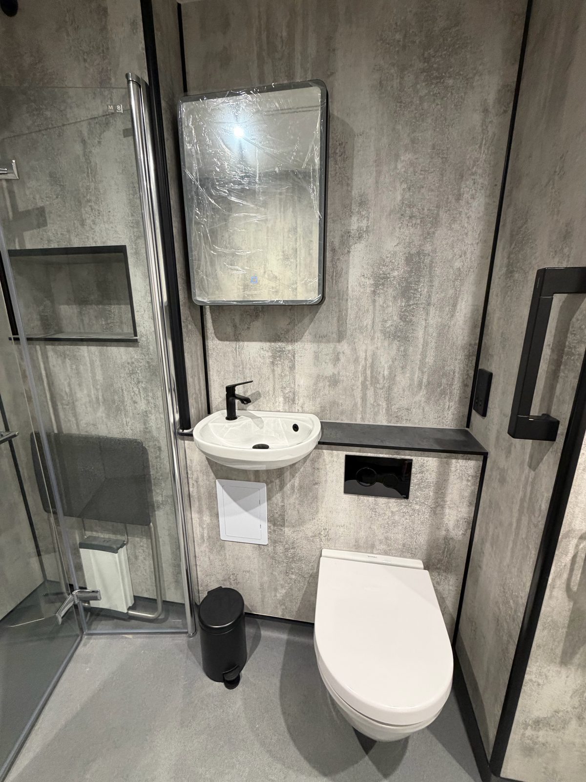 Modern wet room with grey concrete-effect wall panels, glass shower enclosure, WC and basin — EscapeHaus Joinery, Fife