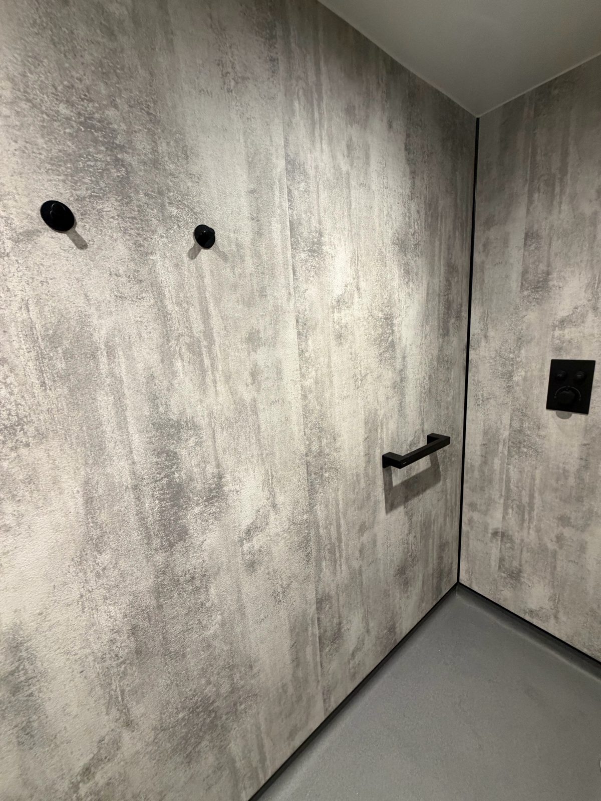 Matte black shower valve and towel hooks on grey concrete-effect wet room wall panels