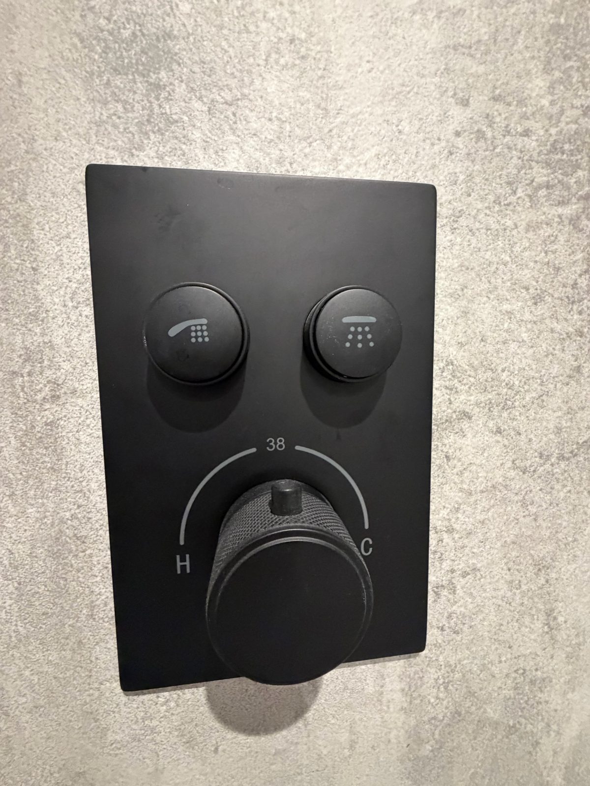 Close-up of matte black thermostatic shower mixer panel on grey wet room wall