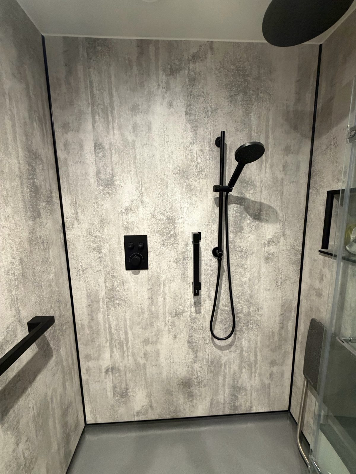 Wet room rainfall shower head and handheld shower on matte black rail against grey wall panels
